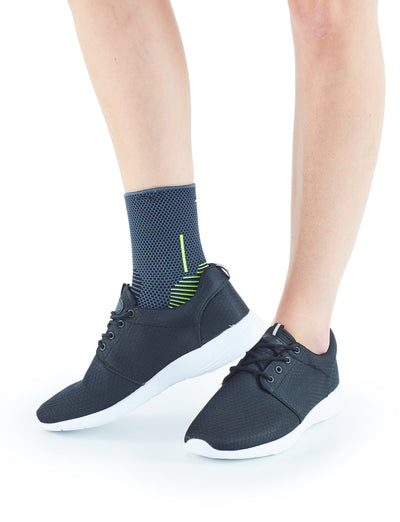 Close-up of a person standing in stylish black sneakers and dark blue ankle socks with Neo G USA Active Ankle Support against a white background.