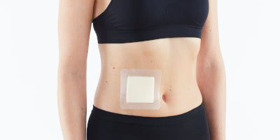 A woman standing with an Opti-Heal Silicone Foam Absorbent Dressing on her abdomen