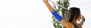 Woman wearing Neo G Airflow Plus Elbow Support with Silicone Joint Cushions and Neo G Wrist Band, stretching arms with resistance band
