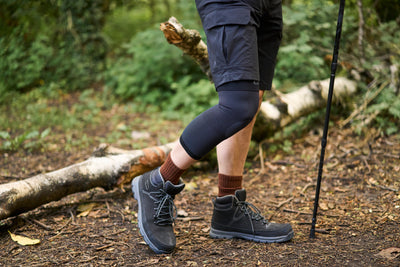 A person with hiking boots and poles, wearing an Airflow knee support. 