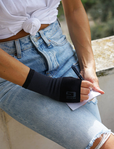 Woman wearing black Neo G Airflow Wrist & Thumb Support on right hand, sitting down, writing