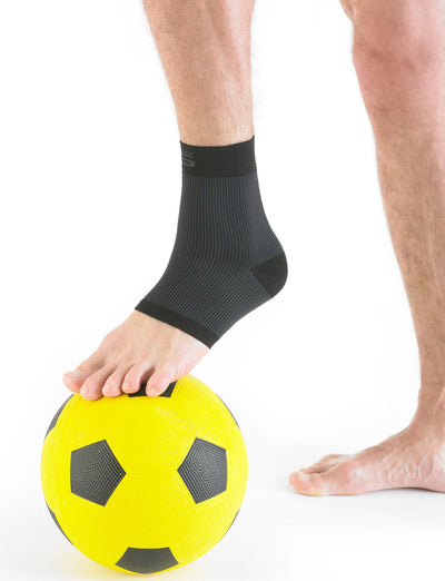 Pair of feet with one wearing black Neo G Airflow Ankle Support resting on a soccer ball