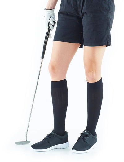 Woman wearing Neo G Energizing Dress Socks with sneakers, holding a golf club